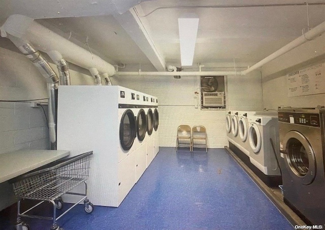 community laundry room featuring concrete block wall, washer and clothes dryer, and a wall mounted air conditioner