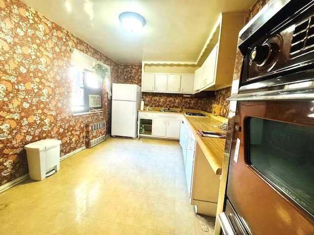 kitchen featuring freestanding refrigerator, oven, white cabinetry, and wallpapered walls