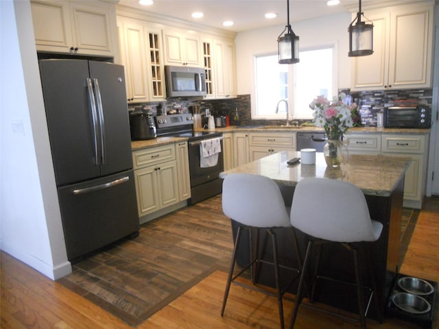 kitchen featuring appliances with stainless steel finishes, decorative light fixtures, a kitchen breakfast bar, a center island, and light stone counters