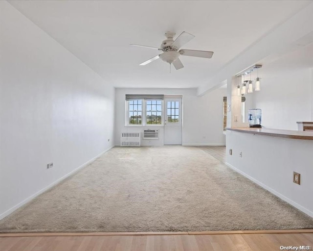 unfurnished living room with light colored carpet, radiator heating unit, a wall unit AC, and ceiling fan