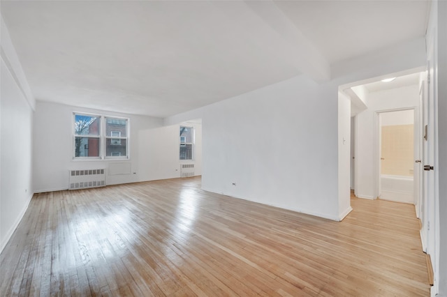 unfurnished living room with beam ceiling, radiator, and light wood-type flooring