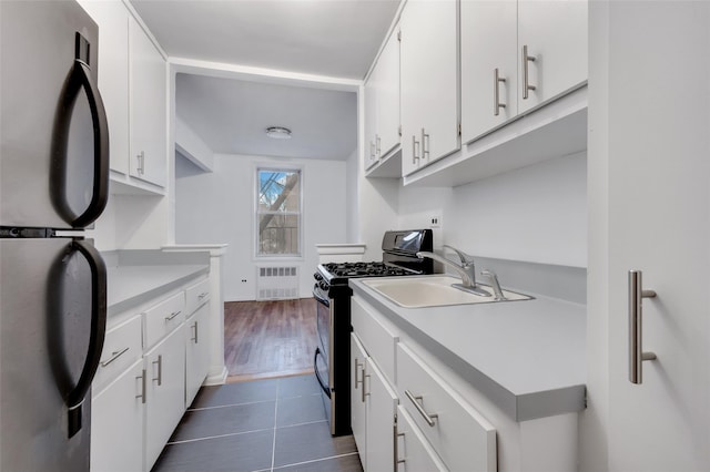 kitchen with radiator, refrigerator, range with gas cooktop, white cabinetry, and dark tile patterned floors