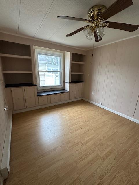 empty room featuring a textured ceiling, light wood-style flooring, built in shelves, and ornamental molding