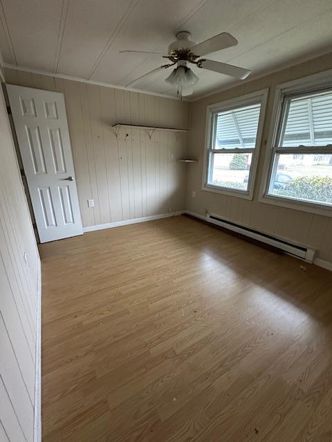 spare room with a ceiling fan, wood finished floors, baseboards, and baseboard heating