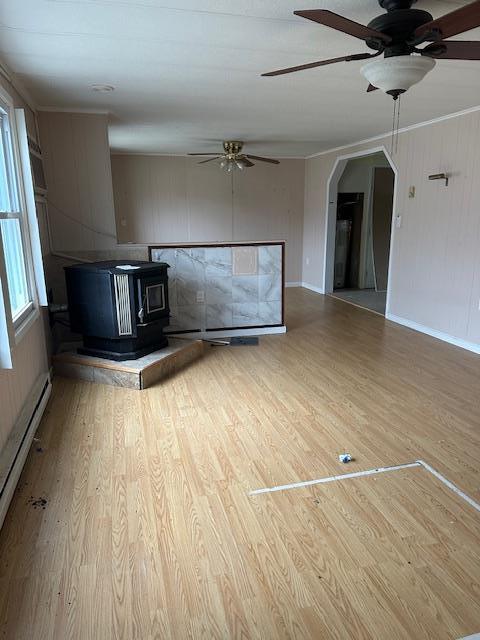 unfurnished living room featuring arched walkways, a baseboard radiator, wood finished floors, and a wood stove