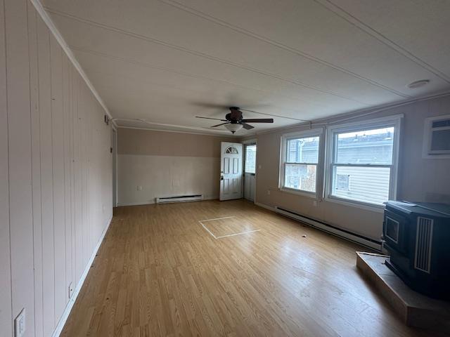 unfurnished living room featuring wood finished floors, a wood stove, ceiling fan, and a baseboard radiator