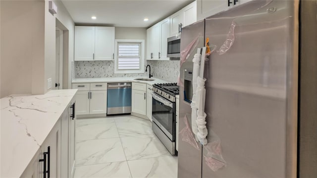 kitchen with sink, white cabinetry, stainless steel appliances, tasteful backsplash, and light stone countertops