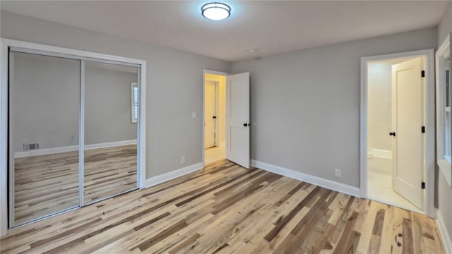 unfurnished bedroom featuring ensuite bathroom, light hardwood / wood-style floors, and a closet