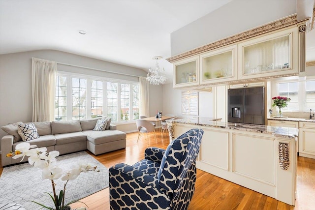 living room featuring a notable chandelier, lofted ceiling, sink, and light wood-type flooring