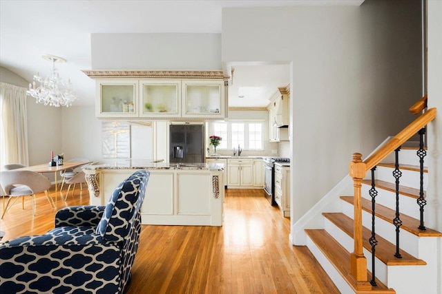 kitchen featuring sink, refrigerator with ice dispenser, hanging light fixtures, light stone countertops, and gas stove