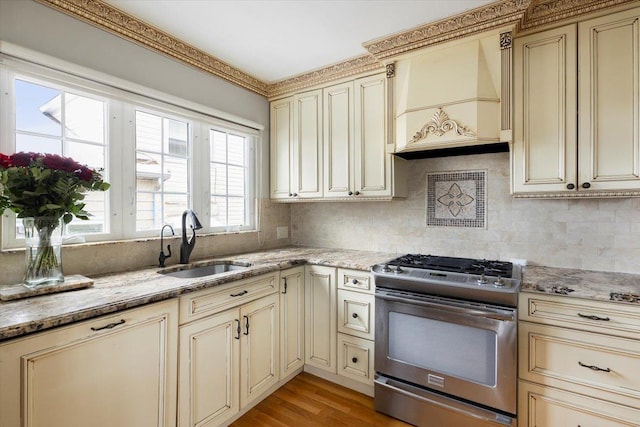 kitchen with sink, decorative backsplash, gas range, light stone countertops, and cream cabinetry