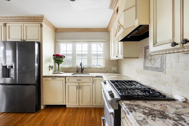 kitchen with sink, light wood-type flooring, cream cabinetry, stainless steel appliances, and wall chimney range hood