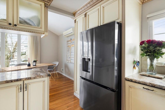 kitchen with stainless steel fridge, light stone counters, and cream cabinetry