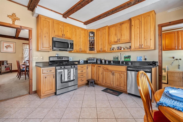 kitchen with appliances with stainless steel finishes, light tile patterned flooring, sink, and beamed ceiling