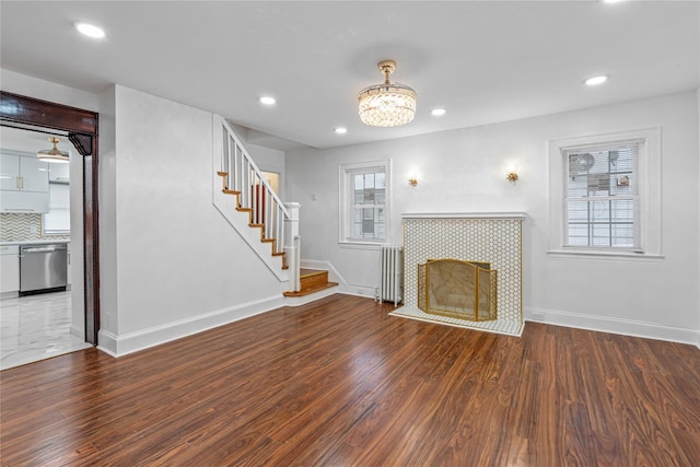 unfurnished living room with hardwood / wood-style flooring, a tile fireplace, radiator, and a healthy amount of sunlight