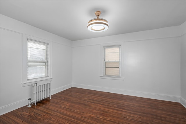 empty room with radiator, a wealth of natural light, and dark hardwood / wood-style floors