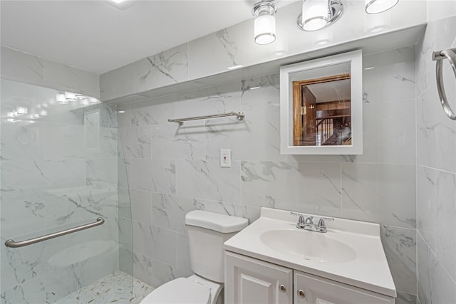 bathroom with a tile shower, vanity, tile walls, and toilet