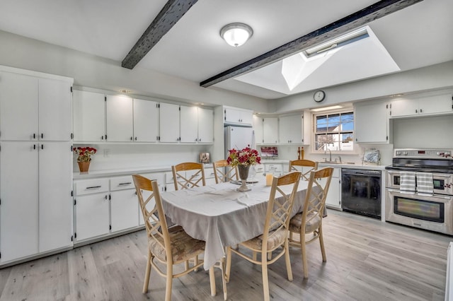 dining space with sink, beam ceiling, a skylight, and light hardwood / wood-style floors