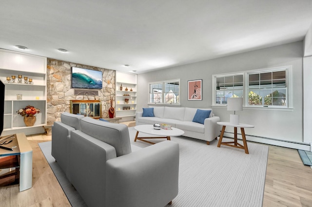 living room featuring a baseboard radiator, light wood-type flooring, a fireplace, and built in shelves