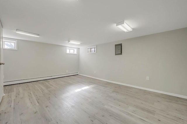 basement featuring a baseboard heating unit, electric panel, and light wood-type flooring