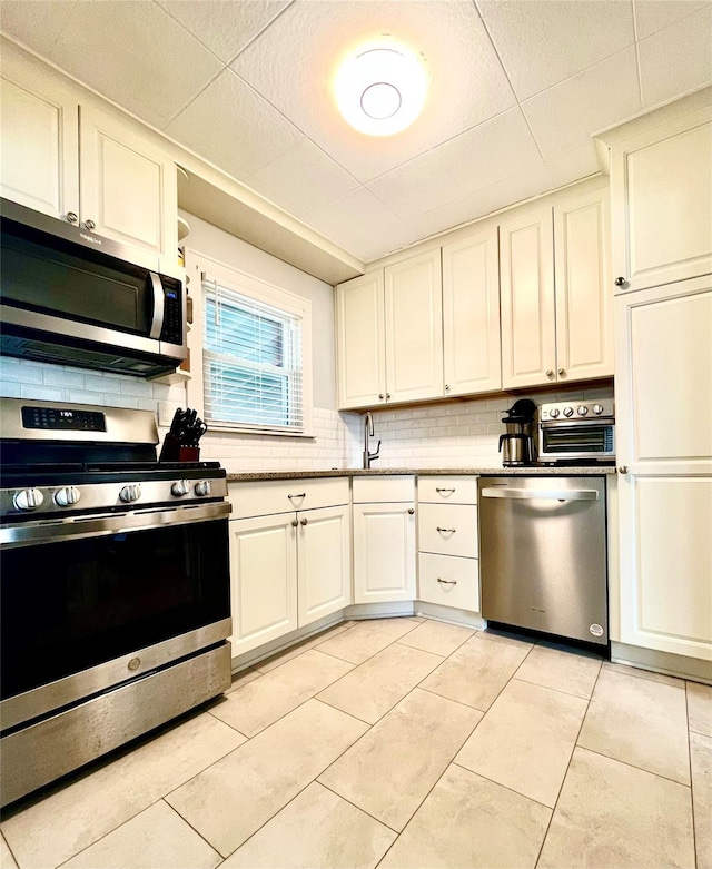 kitchen with light stone countertops, light tile patterned floors, decorative backsplash, white cabinets, and stainless steel appliances