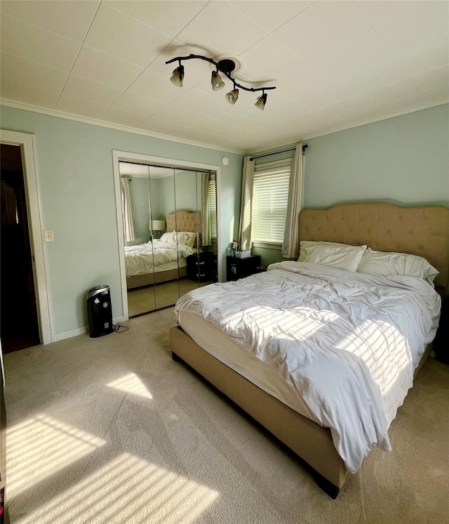 carpeted bedroom with a closet, baseboards, and crown molding