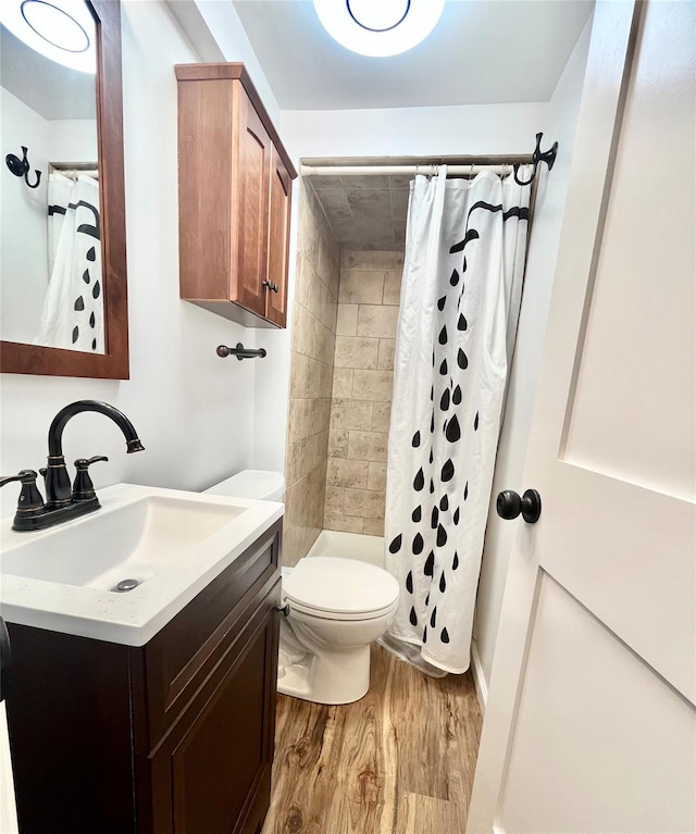 bathroom with a tile shower, toilet, vanity, and wood finished floors