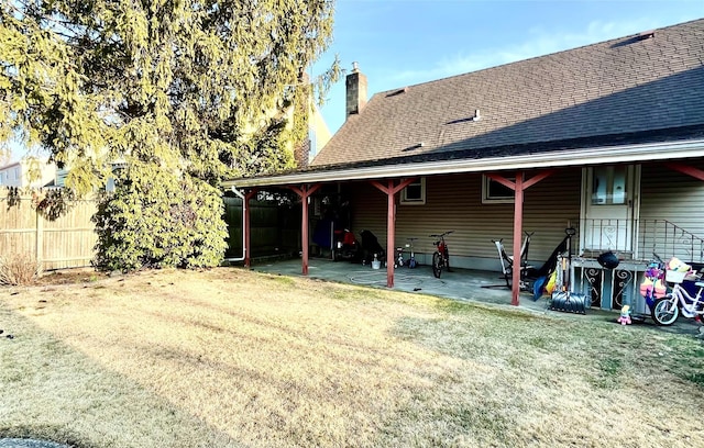 rear view of property with a patio, fence, a yard, a shingled roof, and a chimney