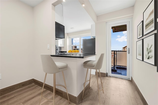 kitchen with a kitchen breakfast bar, dark countertops, wood finished floors, freestanding refrigerator, and a healthy amount of sunlight