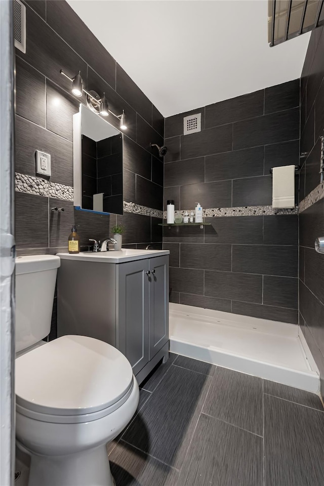 full bathroom featuring visible vents, toilet, vanity, and a tile shower