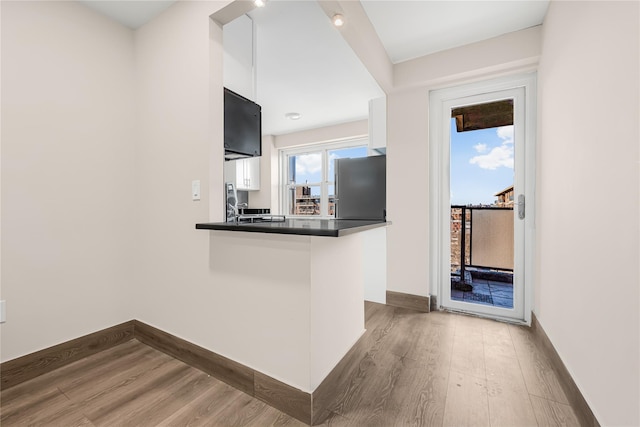 kitchen with dark countertops, wood finished floors, freestanding refrigerator, a peninsula, and white cabinets