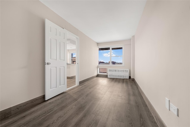 empty room with dark wood-style floors, radiator heating unit, and baseboards