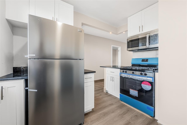 kitchen with stainless steel appliances, dark countertops, white cabinets, and light wood finished floors