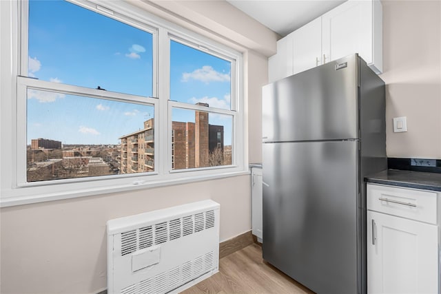 kitchen featuring light wood-style flooring, dark countertops, white cabinetry, freestanding refrigerator, and radiator