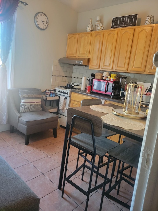 kitchen featuring gas range, light brown cabinetry, light tile patterned flooring, and decorative backsplash