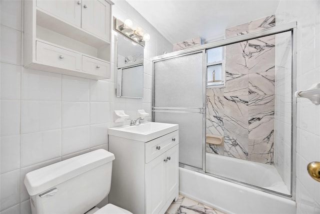 full bathroom featuring vanity, toilet, combined bath / shower with glass door, and tile walls