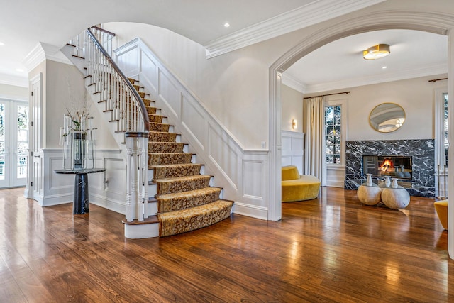 stairs featuring arched walkways, crown molding, wood-type flooring, a decorative wall, and a high end fireplace