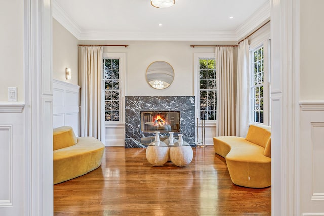 living area with wainscoting, ornamental molding, wood finished floors, a fireplace, and a decorative wall