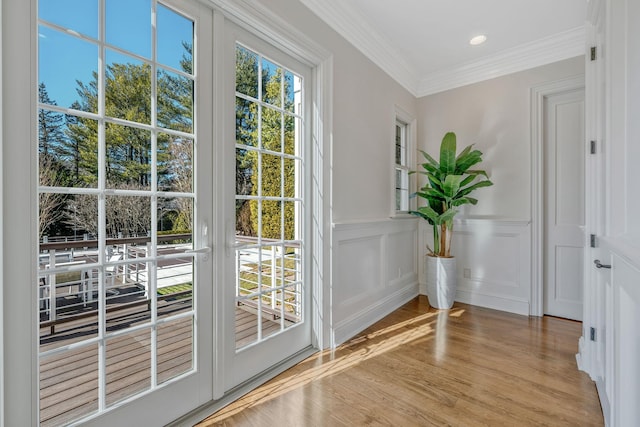 doorway with recessed lighting, a wainscoted wall, a decorative wall, ornamental molding, and light wood finished floors