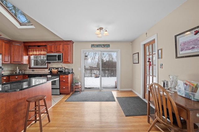 kitchen with stainless steel appliances, light hardwood / wood-style floors, dark stone countertops, a kitchen bar, and decorative backsplash