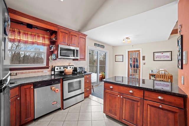 kitchen with appliances with stainless steel finishes, vaulted ceiling, light tile patterned flooring, dark stone counters, and tasteful backsplash