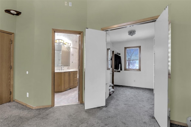 unfurnished bedroom featuring a baseboard radiator, connected bathroom, sink, and light colored carpet