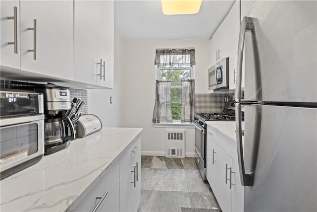 kitchen featuring stainless steel appliances, light stone countertops, decorative backsplash, and white cabinets