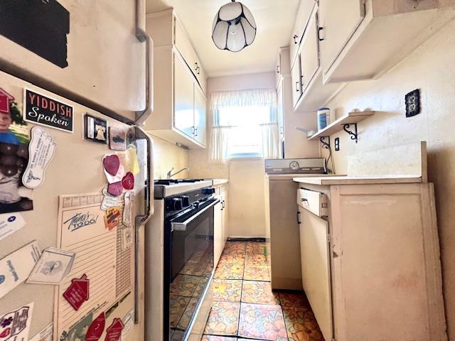 kitchen with washer / dryer, white fridge, black gas range oven, and white cabinets