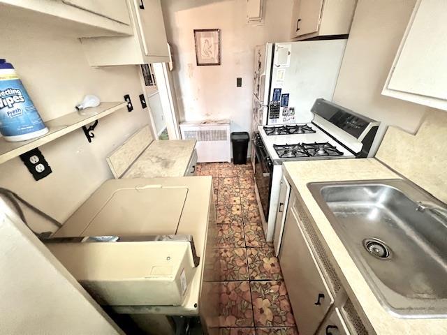 kitchen with sink, refrigerator, radiator, gas range oven, and white cabinets