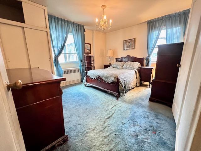 carpeted bedroom with an inviting chandelier and radiator heating unit