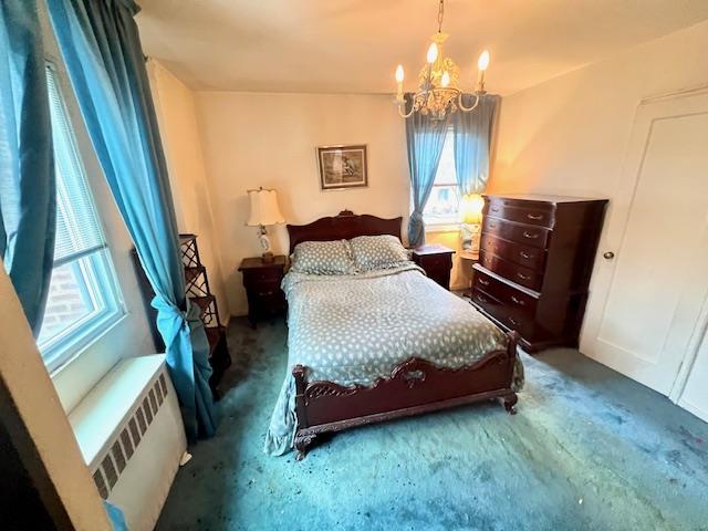 bedroom with radiator heating unit, a chandelier, and carpet flooring