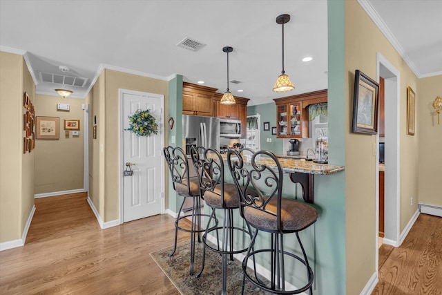 kitchen featuring visible vents, light stone countertops, appliances with stainless steel finishes, a kitchen breakfast bar, and brown cabinetry