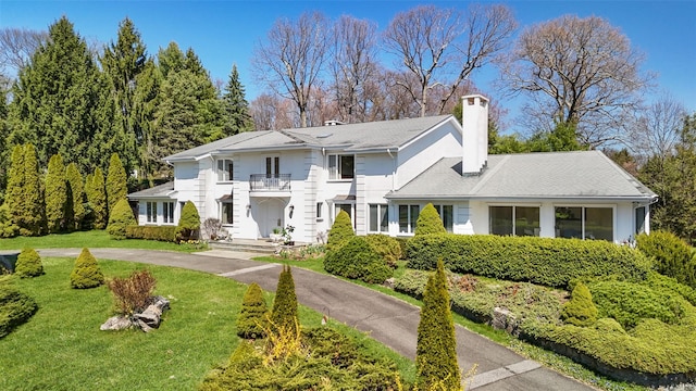 greek revival inspired property with a front yard, a chimney, curved driveway, and a balcony