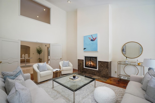 living room with a high ceiling, a premium fireplace, baseboards, and wood finished floors